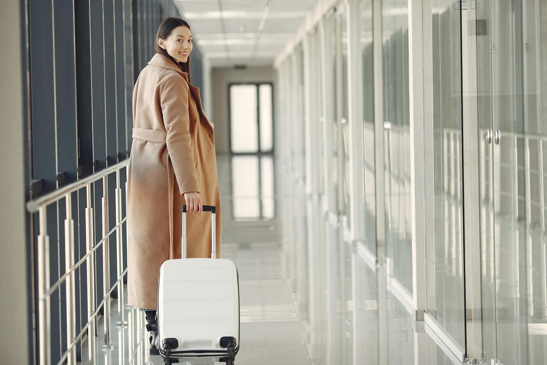 Smiling woman traveler with suitcase in airport hallway